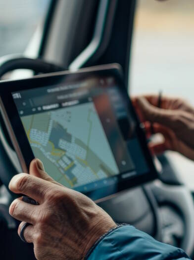 A man is seated in the drivers seat of a truck, using a tablet for navigation or communication purposes