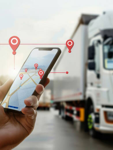 Close-up of a hand holding a smartphone with a GPS tracking app against trucks