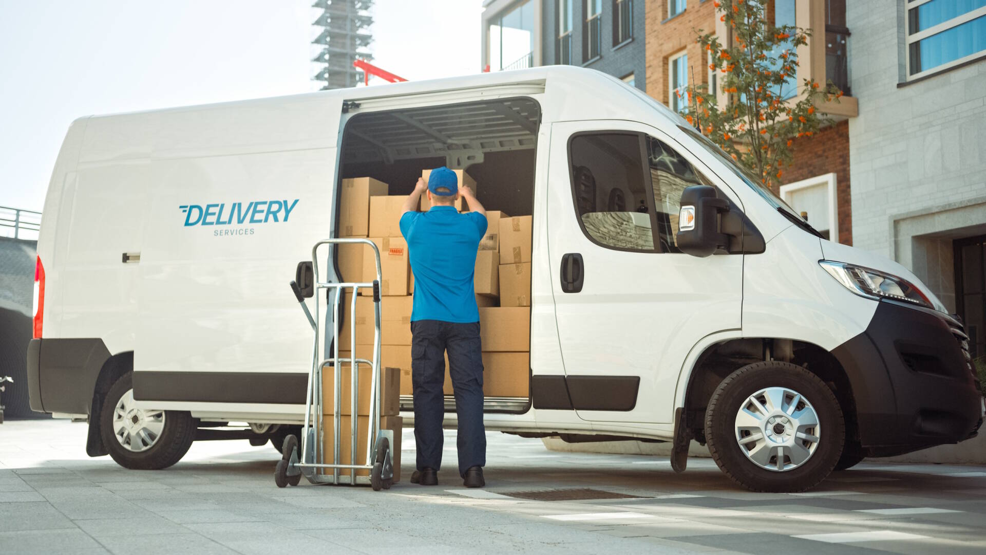 Delivery Man Uses Hand Truck Trolley Full of Cardboard Boxes